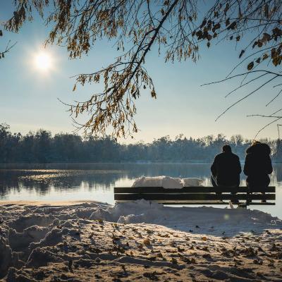 Ein Paar sitzt mit auf einer Bank mit dem Blick auf den See und bewundert den Sonnenuntergang.