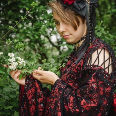 Junge Frau im roten Kleid bewundert weiße Blüte im Wald