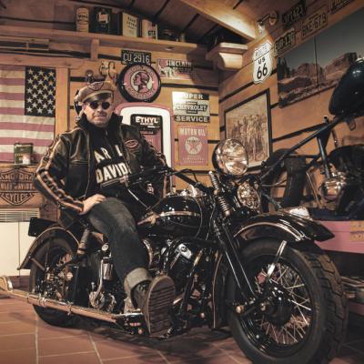 Ein Biker sitzt zurückgelehnt auf seiner Harley Davidson, leicht grinsend, in einer Garage.