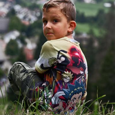 Kleiner Junge sitzt am Berggipfel und blickt über die Schulter